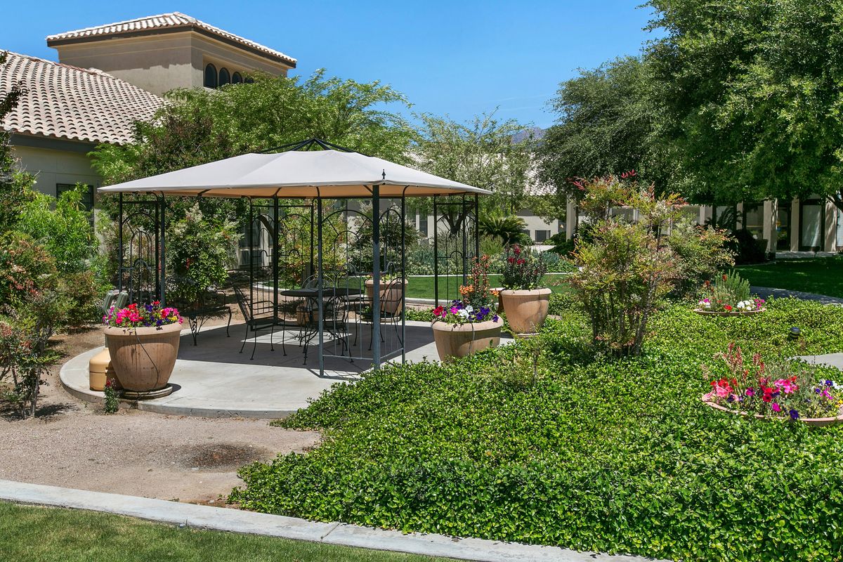 A charming gazebo surrounded by lush greenery and potted plants on a sunny day.