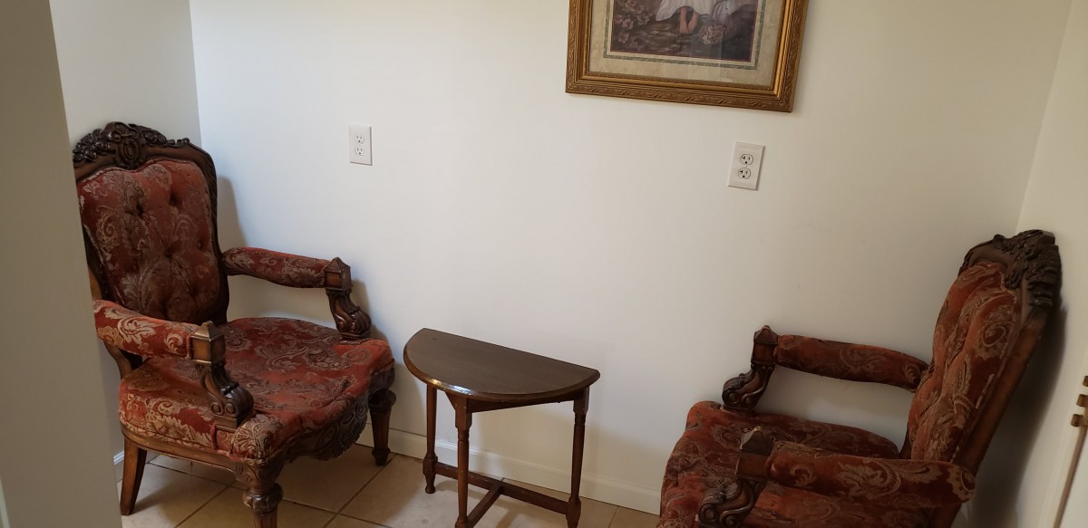 A cozy corner with vintage chairs and a small wooden table, complemented by a framed painting on the wall.