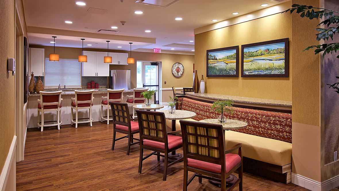 A cozy cafe interior with tables and chairs arranged neatly, featuring artwork on the walls and warm lighting.