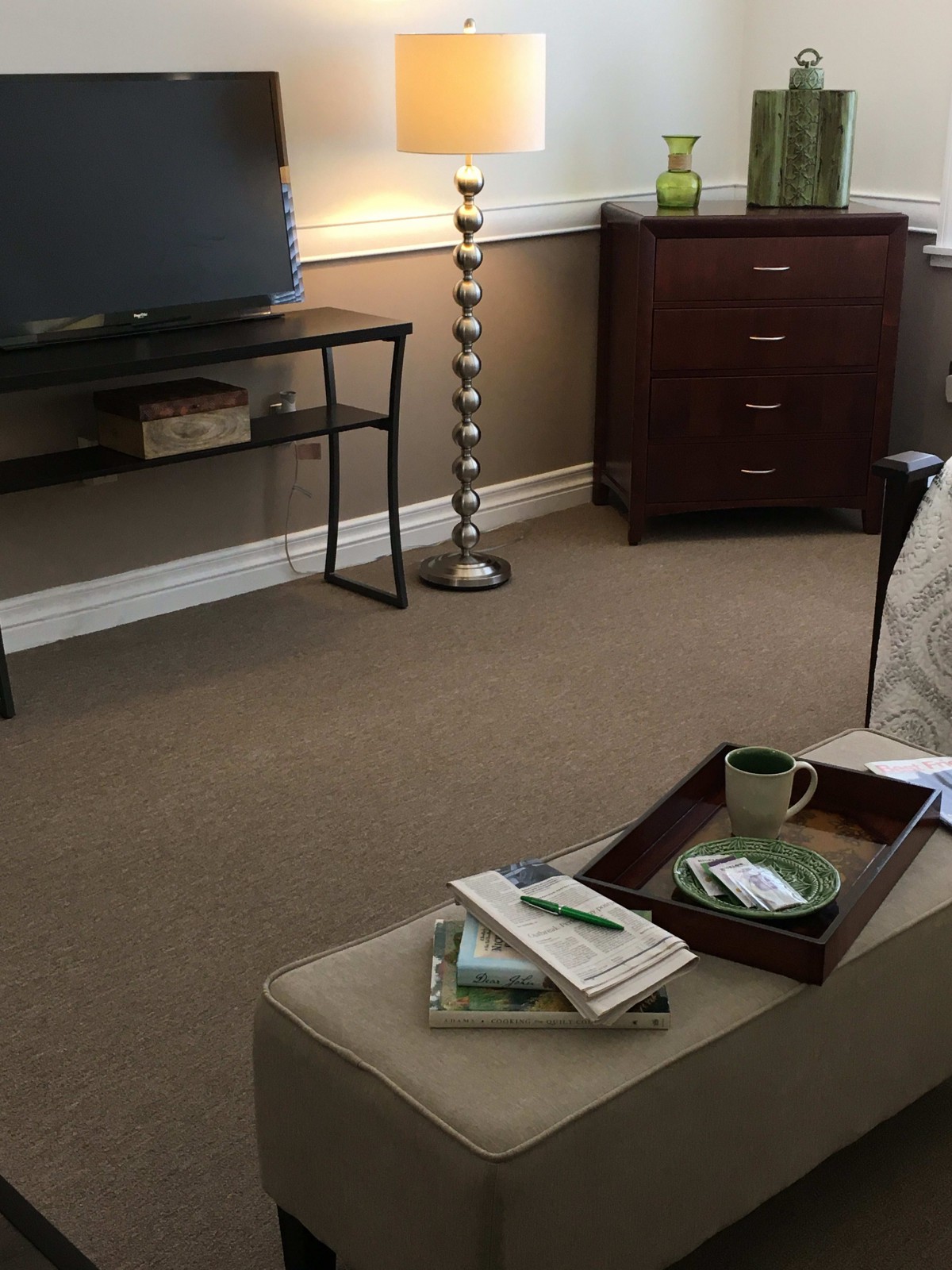 A cozy living room with a TV stand, a floor lamp, and a small table displaying various items.
