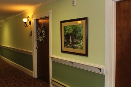 A warmly lit hallway featuring a framed painting on the wall and a door with a wreath.