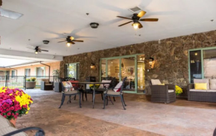 A spacious outdoor patio area with tables, chairs, and ceiling fans, set against a stone wall backdrop.