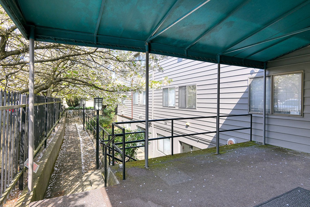 A residential balcony with an awning overlooking a pathway and surrounding greenery.