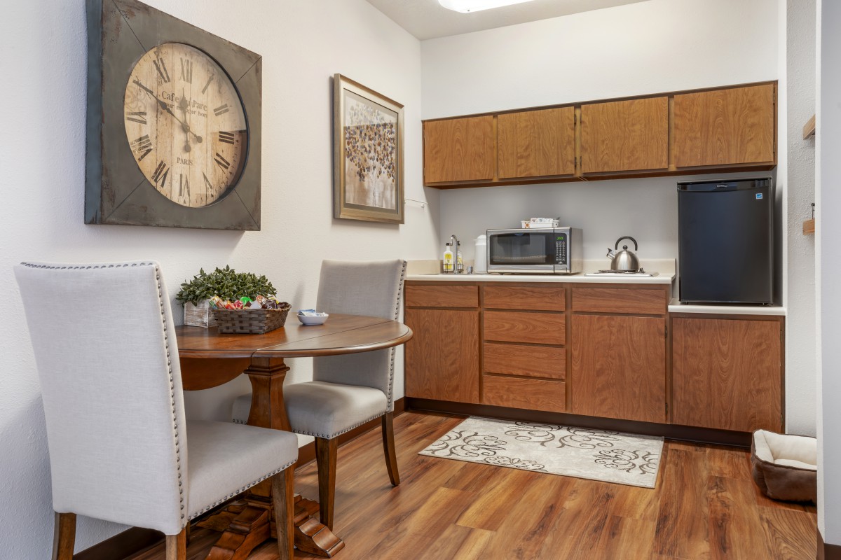 A cozy kitchen area featuring wooden cabinets, a microwave, a small dining table with chairs, and decorative elements.