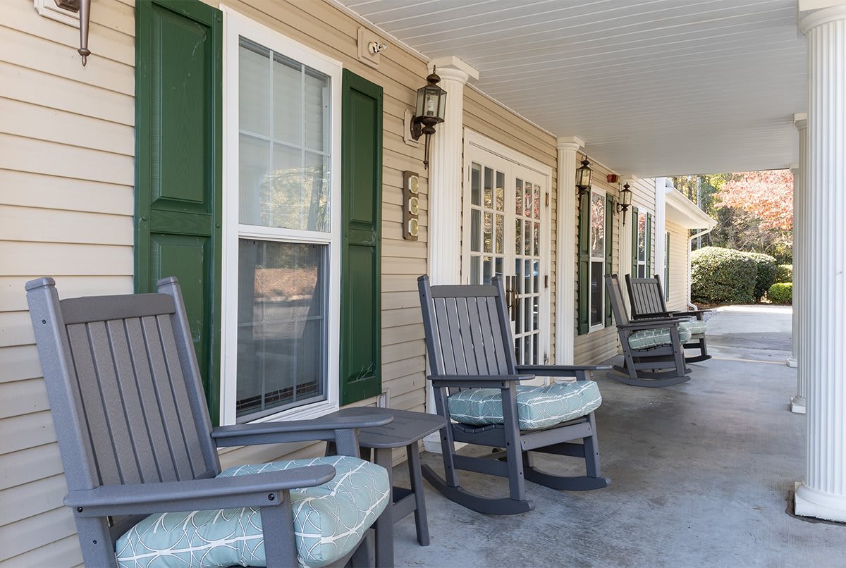 A cozy porch with several rocking chairs lined up outside a house.