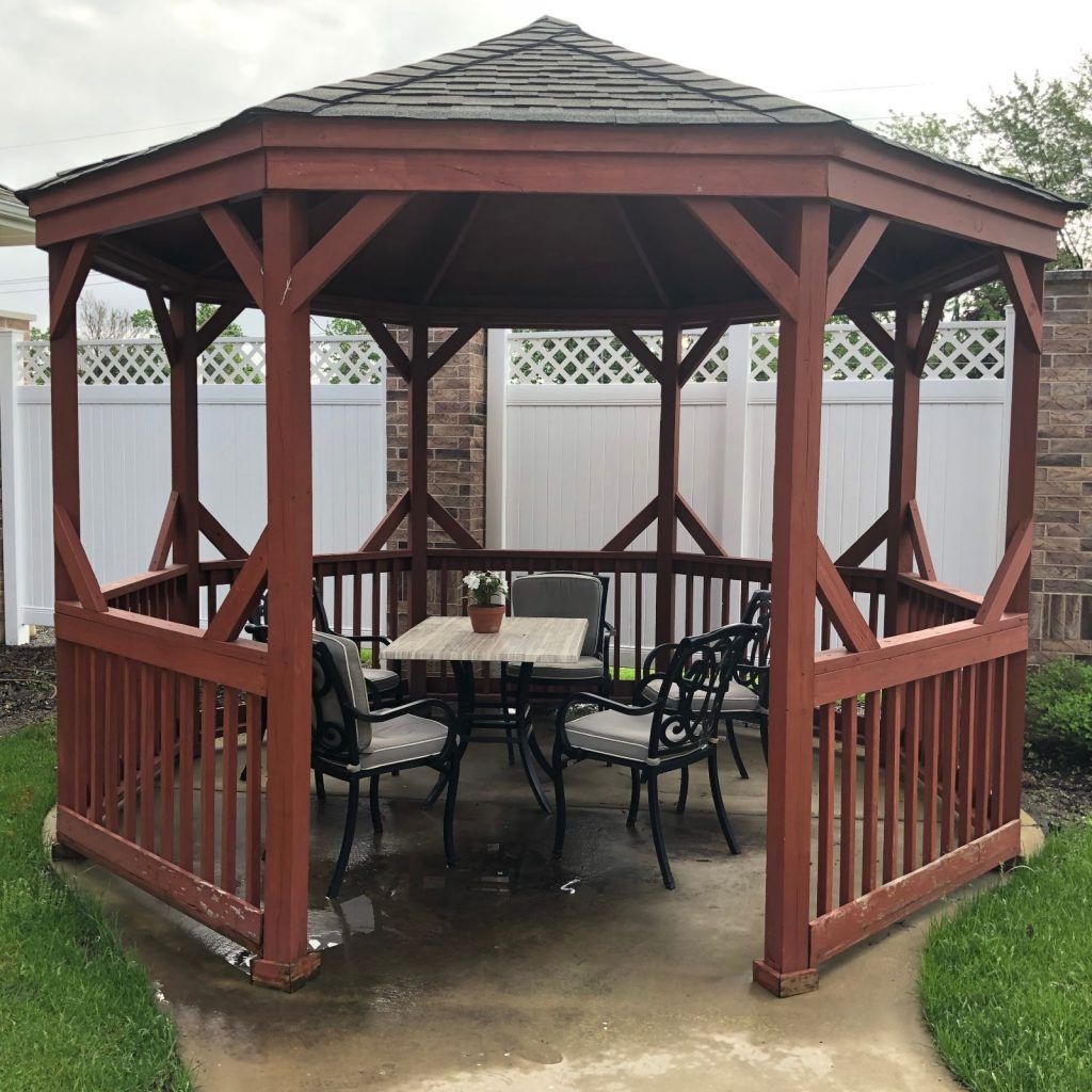 A wooden gazebo with seating and a table inside, set in an outdoor area.