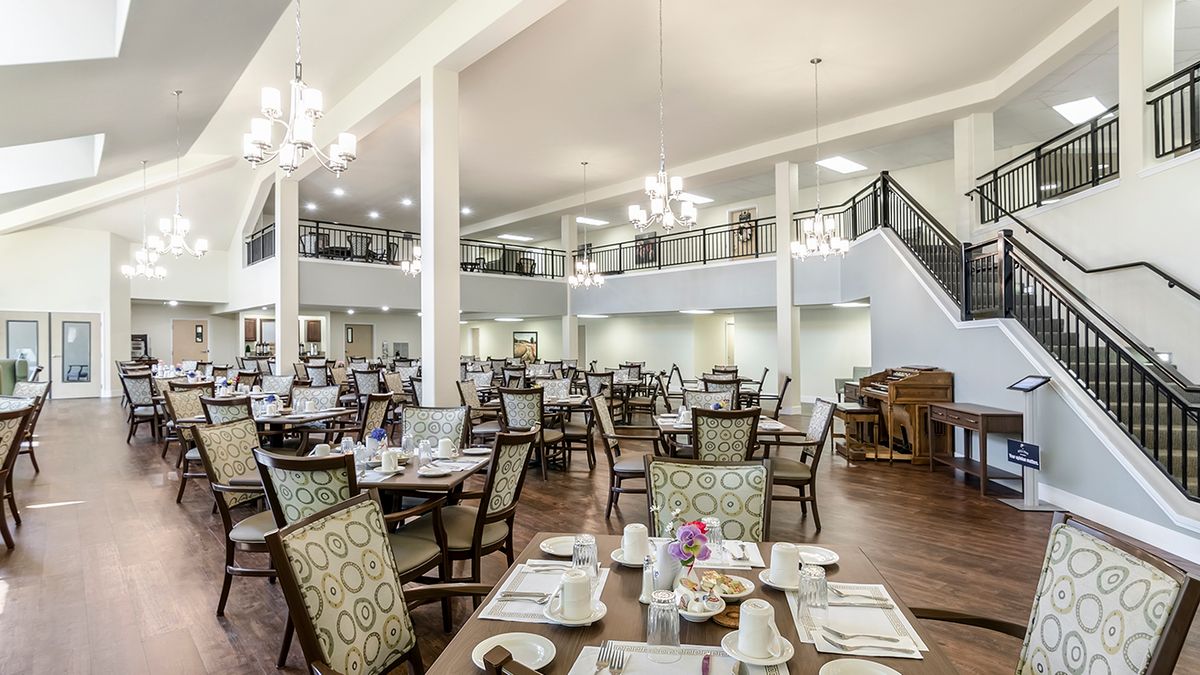 A spacious and elegantly designed dining area with multiple tables and chairs, featuring chandeliers and a mezzanine level.