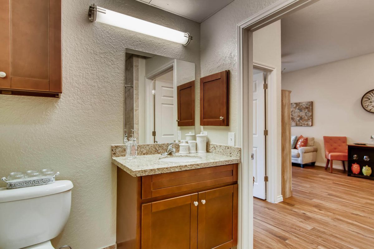 A modern bathroom with a mirror, sink, and wooden cabinet under bright lighting.