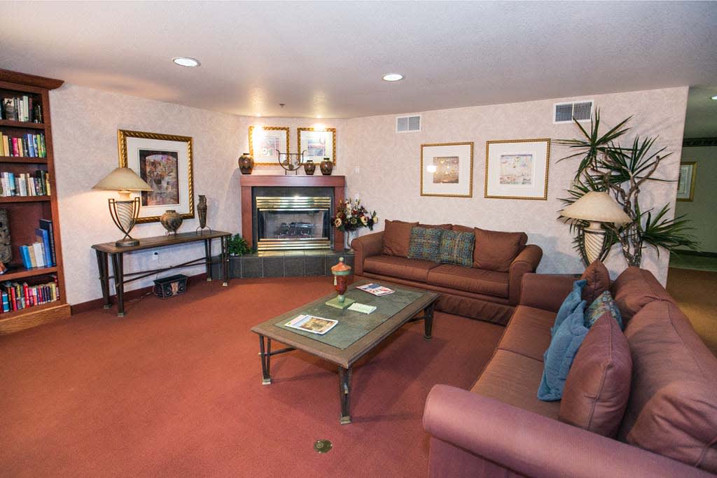 A cozy living room with sofas, a coffee table, and a fireplace, decorated with artwork and plants.