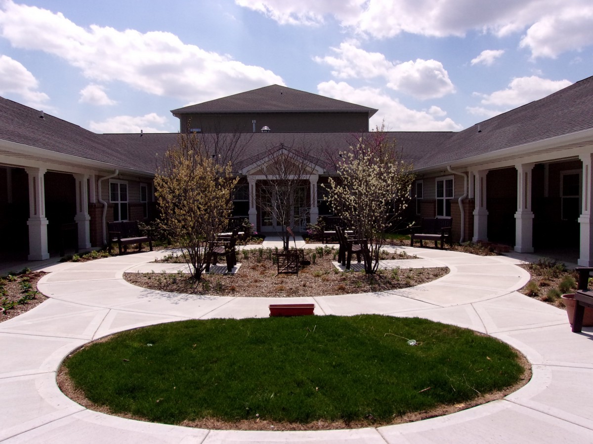 A courtyard featuring a central lawn area with young trees, surrounded by a building under a cloudy sky.