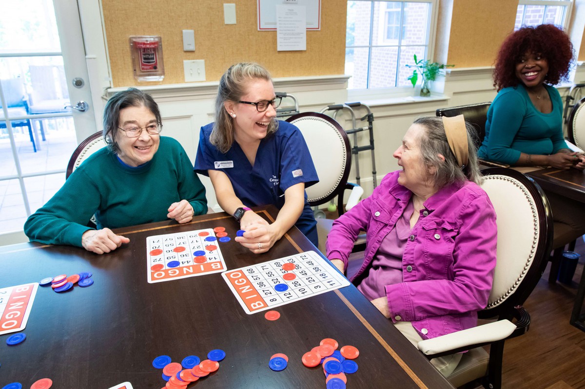 A caregiver enjoying a game of bingo with two elderly women, all smiling and engaging in a lively interaction.