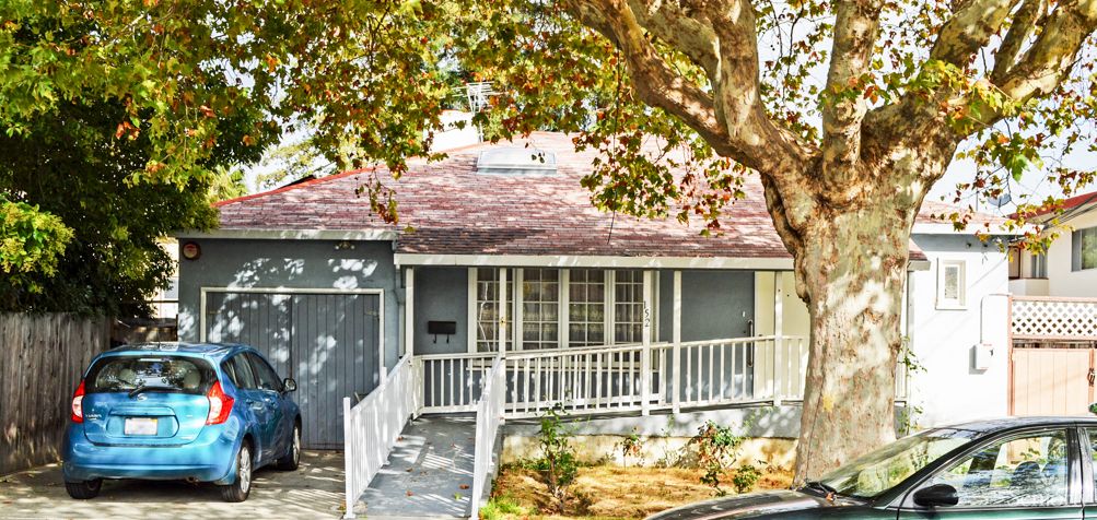 A quaint suburban house with a front porch and a tree-shaded yard.