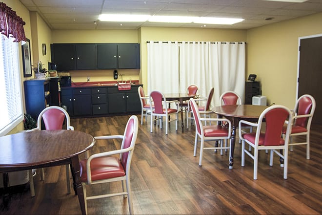 An empty dining area with several tables and chairs, featuring wooden flooring and cabinets.