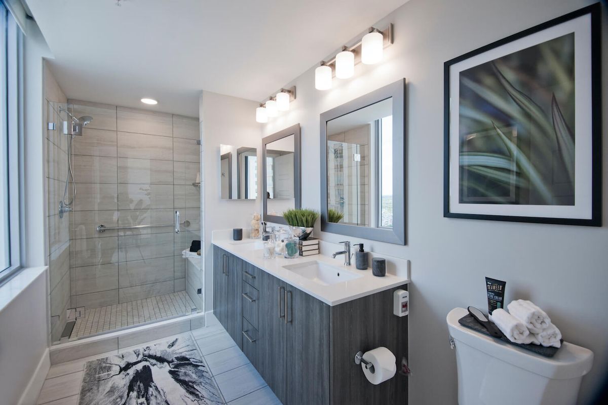 A modern bathroom featuring a double sink vanity with mirrors, decorative lighting, and a spacious shower area.