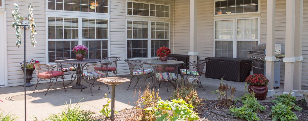 A cozy patio with a table and chairs, adorned with red flowers, set against a background of large windows.