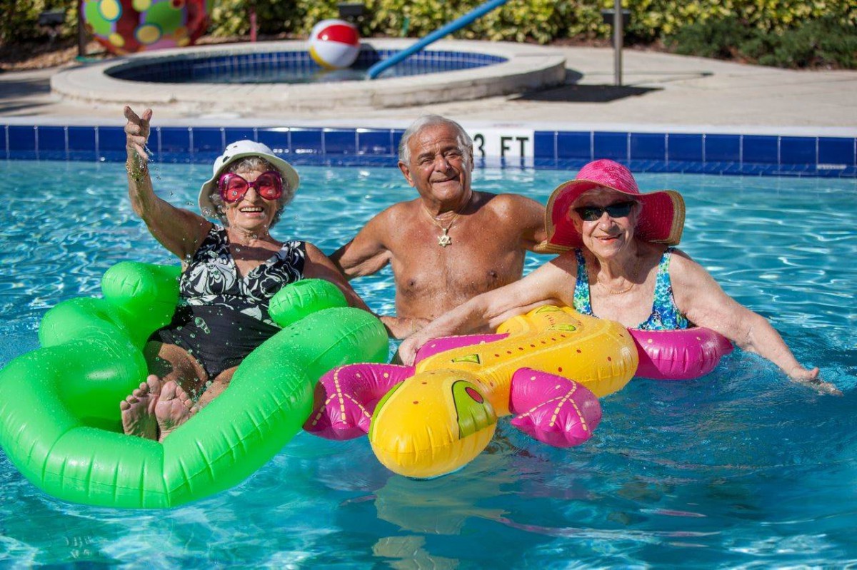 A group of seniors enjoying a sunny day in the pool with inflatables and sun hats.