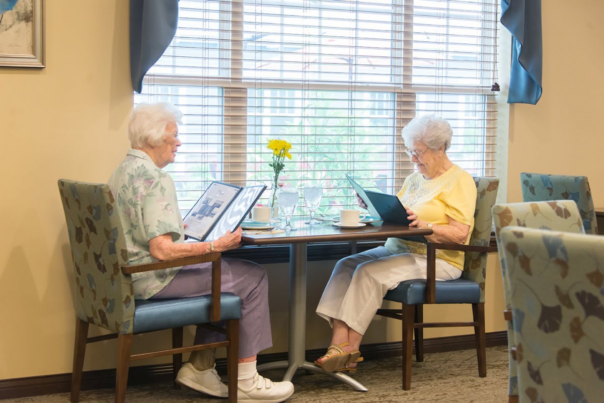 Two elderly women sitting at a table in a restaurant, looking at menus.