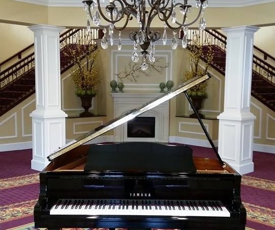 A grand piano in a luxurious interior with a chandelier and staircase.
