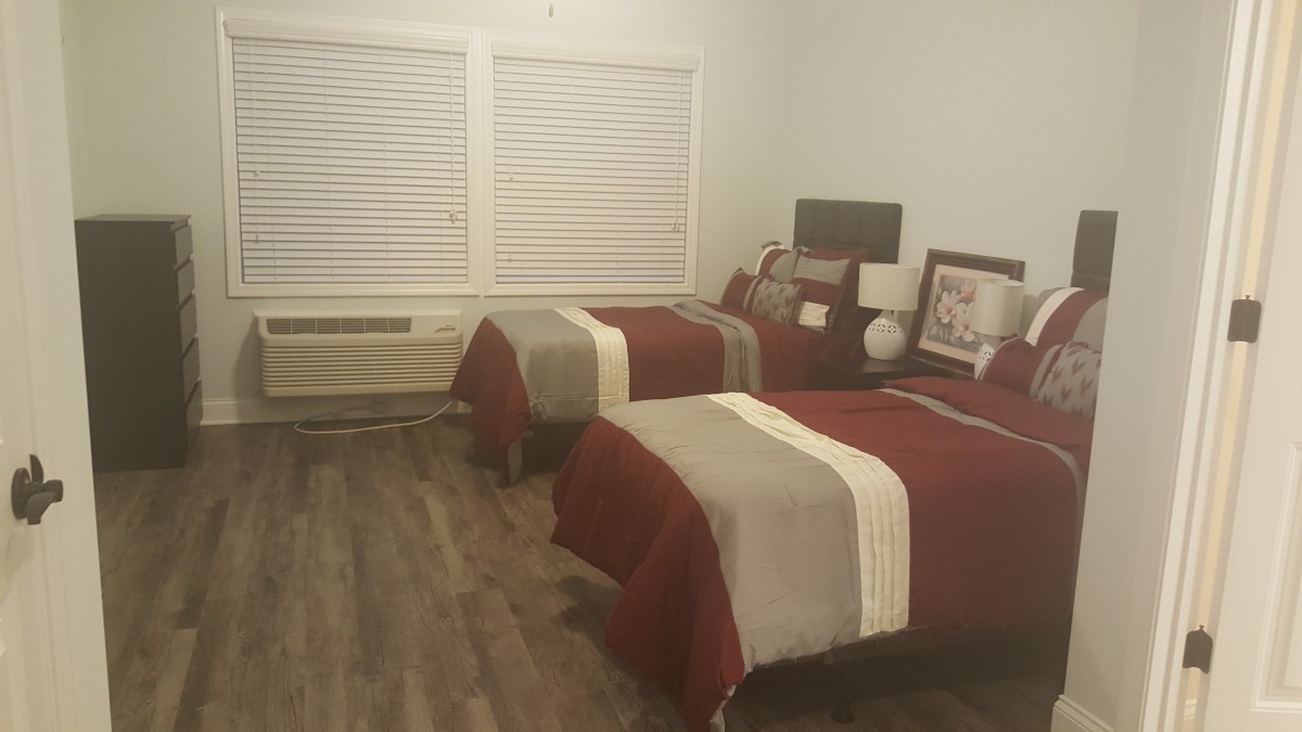 A cozy bedroom with two twin beds, each adorned with red and beige bedding, featuring wooden flooring and window blinds.