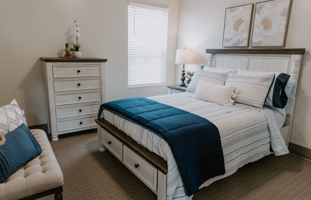 A cozy and modern bedroom featuring a neatly made bed with a blue throw, a white dresser, and soft lighting.