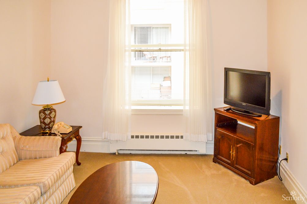 A cozy living room with a sofa, table, lamp, and a television near a bright window.