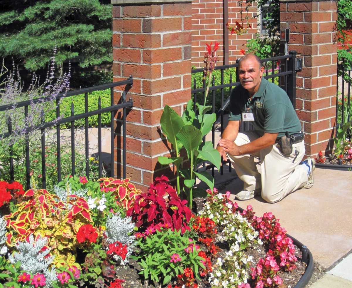 A person kneeling next to a vibrant flower bed in a garden.