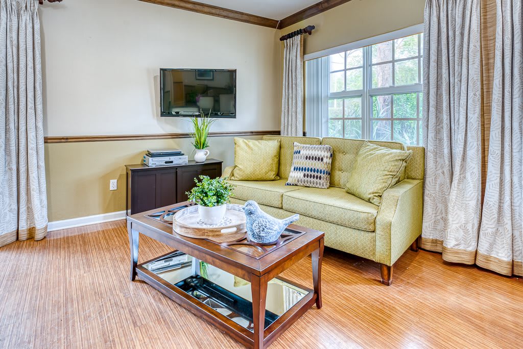 A cozy living room featuring a yellow sofa, glass coffee table, and wall-mounted television.