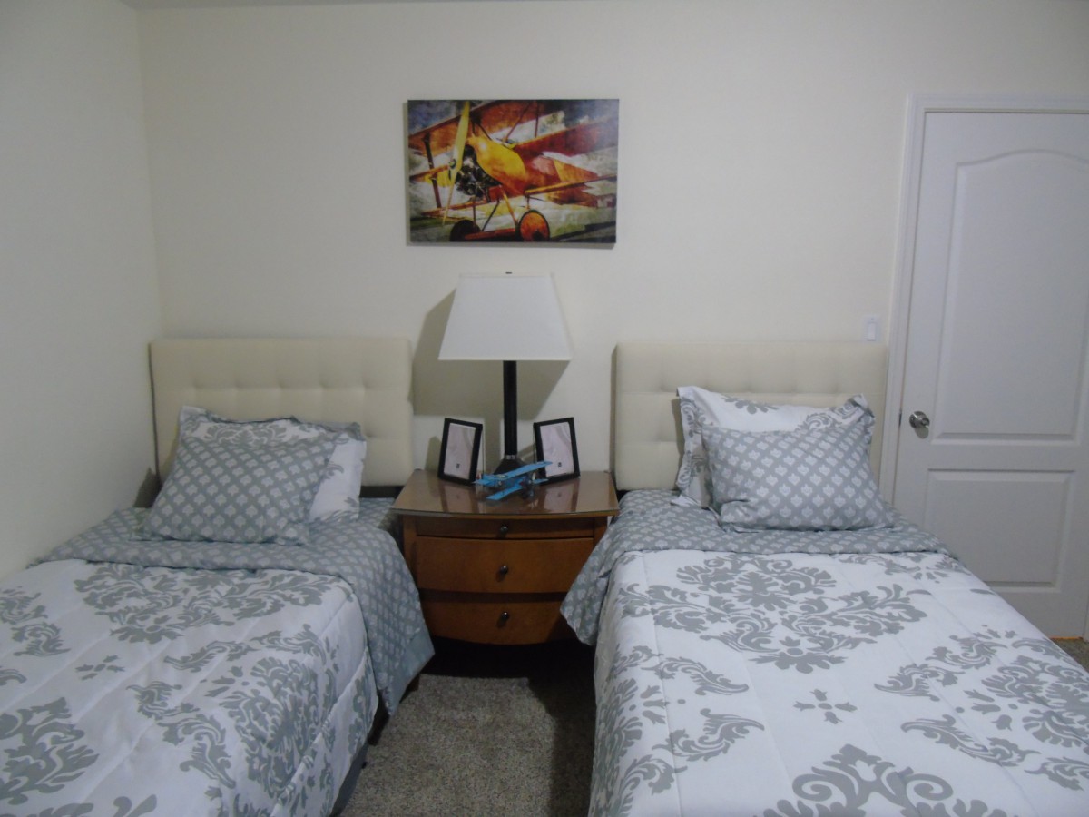 A cozy bedroom with twin beds and a nightstand accompanied by a lamp and decorative artwork.