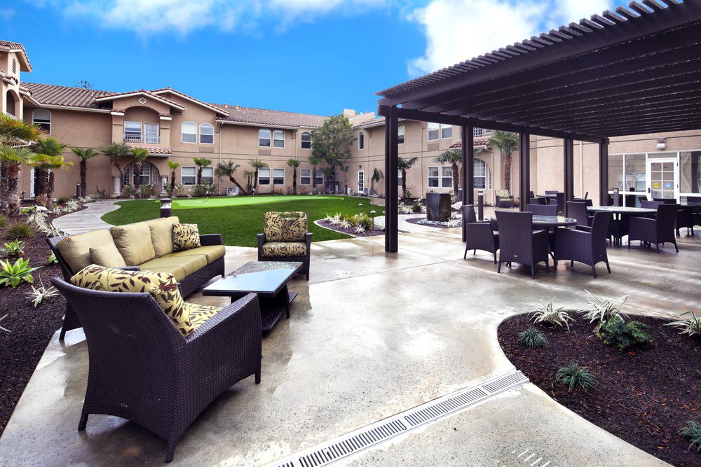 A modern patio area with comfortable seating and a pergola, set against a landscaped garden and residential building.