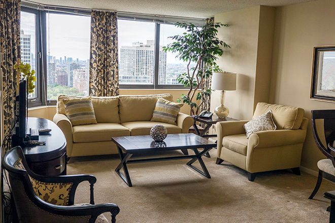 A cozy living room with a sofa, armchair, and coffee table, featuring a large window with a city view.