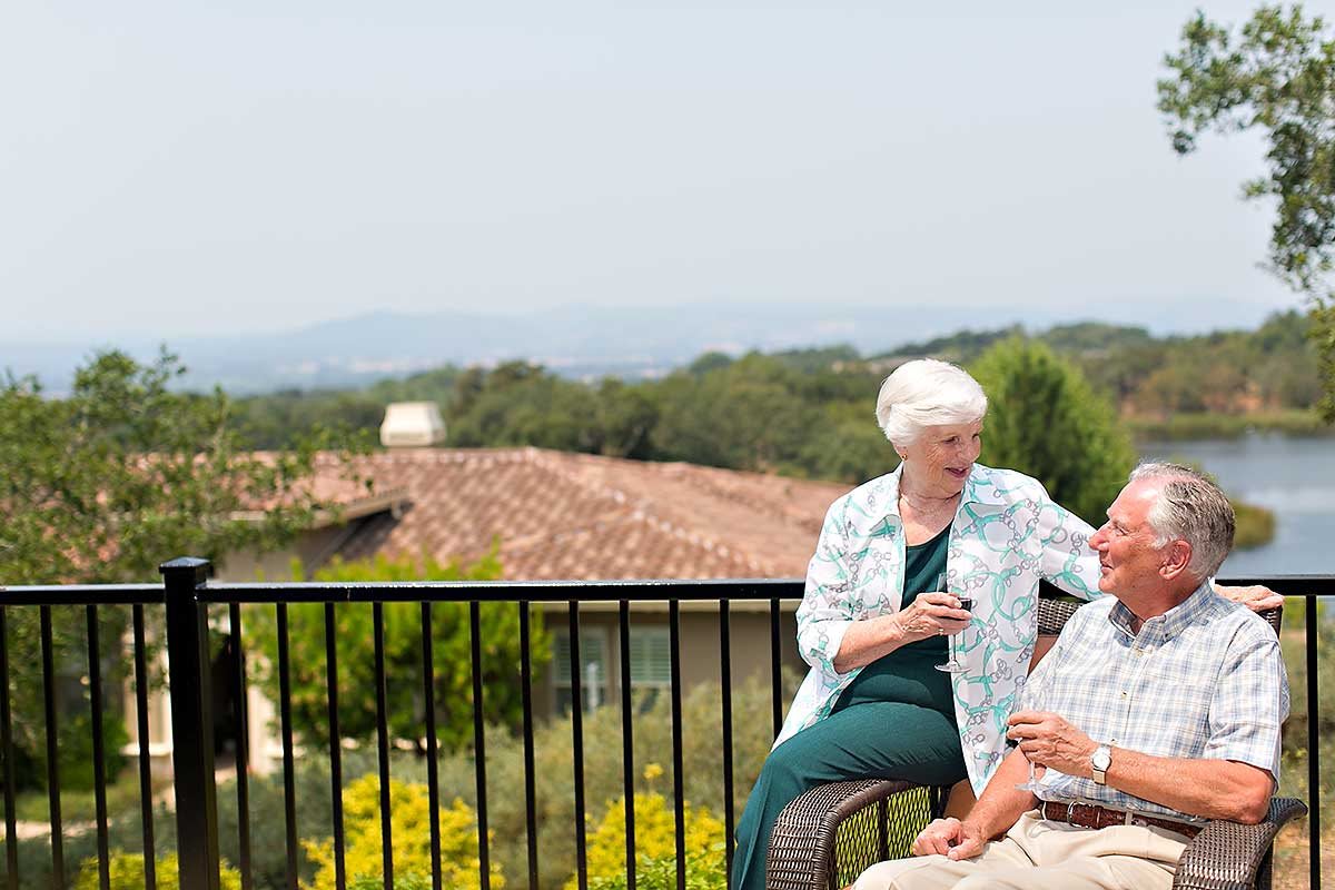 Two seniors having a conversation on a balcony with a scenic view.