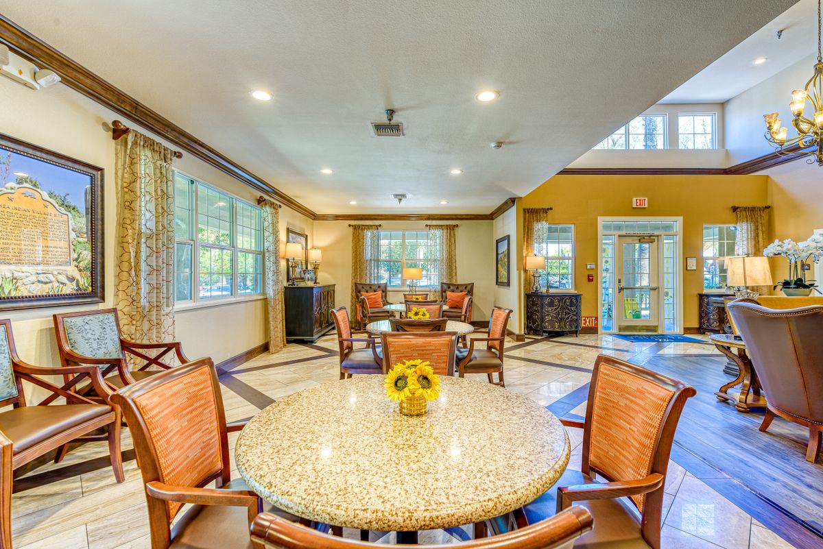 A spacious and well-lit dining area with a round table and wooden chairs, featuring large windows and elegant decor.