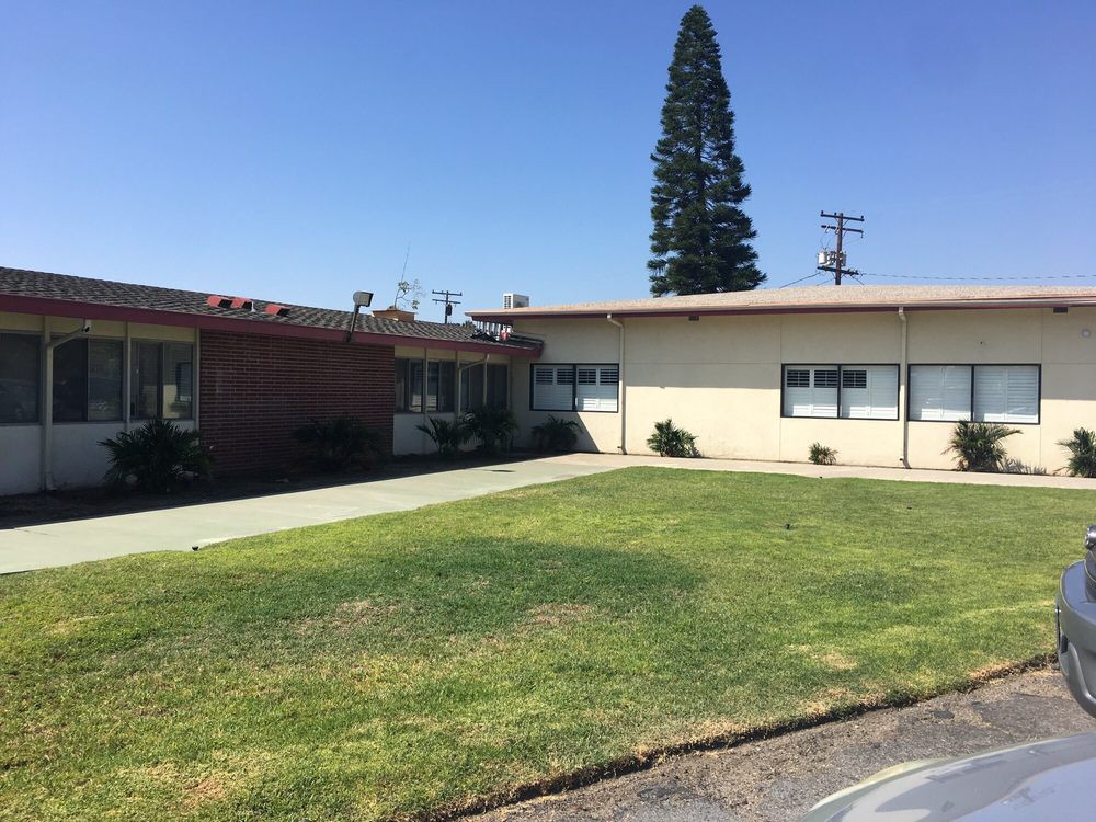 A small, single-story building with a well-maintained lawn and a tall tree in the background under a clear blue sky.