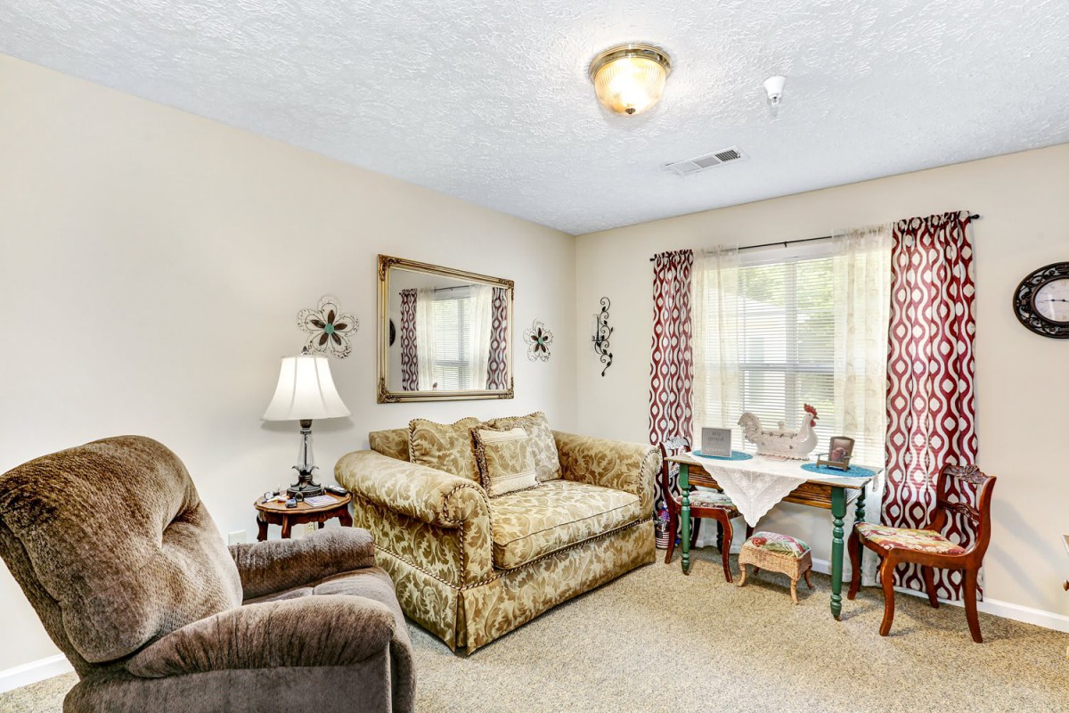 A cozy living room with a patterned sofa, armchair, and a small dining area by the window.