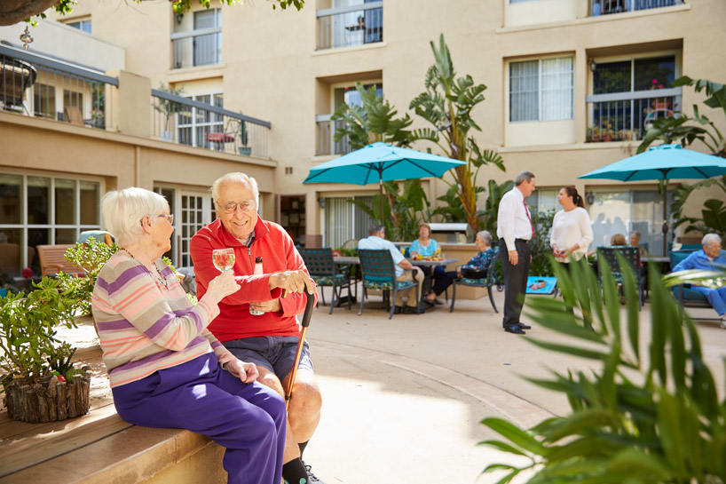 Seniors enjoying a conversation in a sunny courtyard setting.