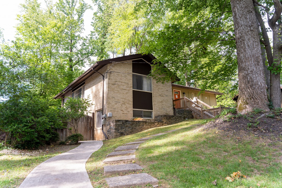 A modern house surrounded by trees, featuring a sloped driveway.