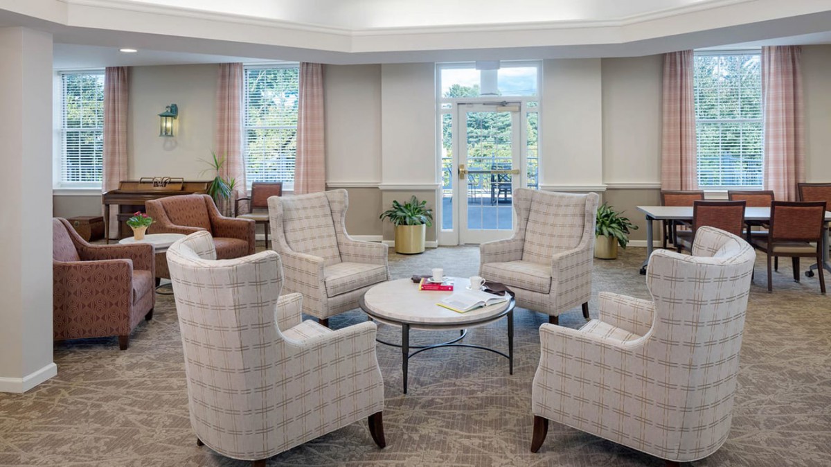 A cozy living room setup with armchairs around a coffee table, plants, and ample natural light from large windows.