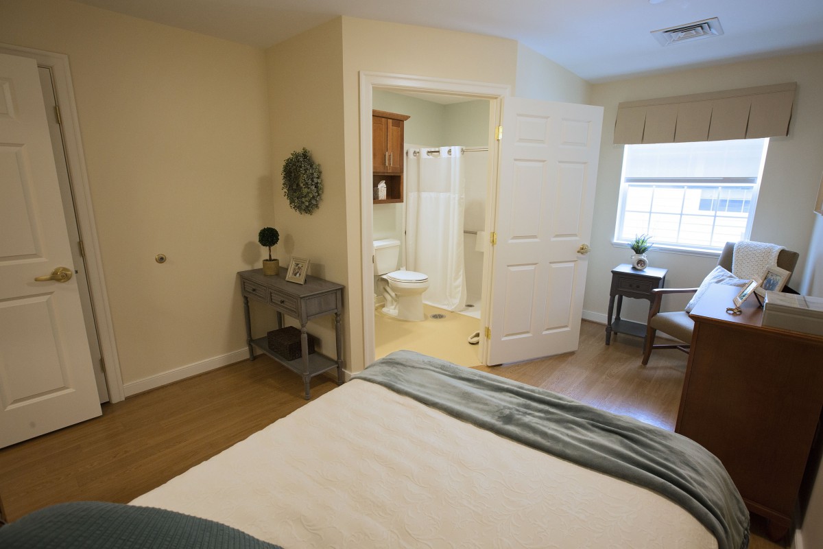 A cozy bedroom with an adjacent bathroom, featuring natural light and simple decor.