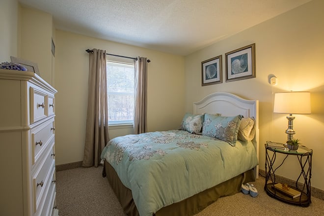 A cozy bedroom with a bed, lamp, and window dressed in curtains.