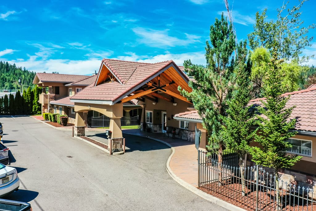A welcoming building entrance with a covered driveway and surrounding greenery under a clear blue sky.