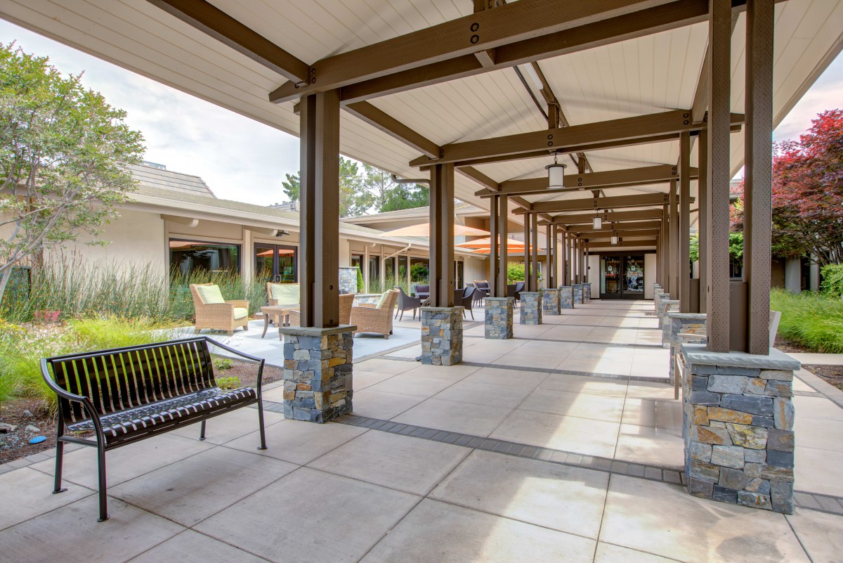 A modern covered walkway with stone columns and benches on either side.