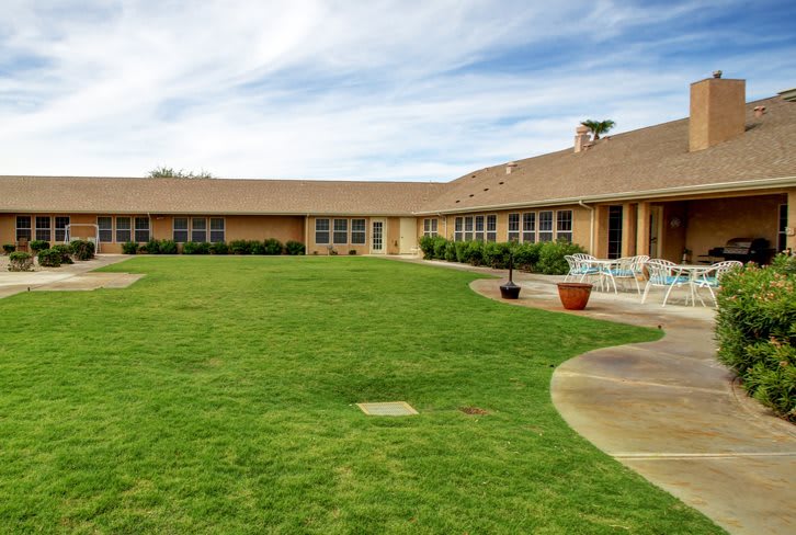 A spacious backyard with a green lawn and patio furniture, surrounded by a one-story house.