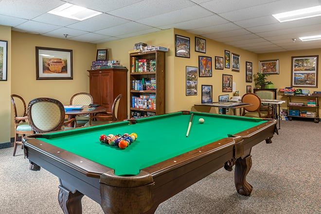 A cozy game room featuring a pool table with green felt, surrounded by framed pictures and a bookcase.