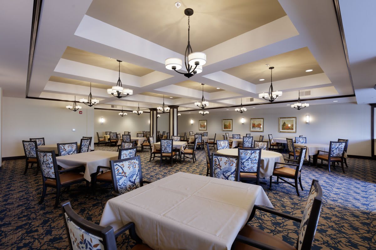 An elegant dining room with neatly arranged tables and chairs, illuminated by chandeliers.