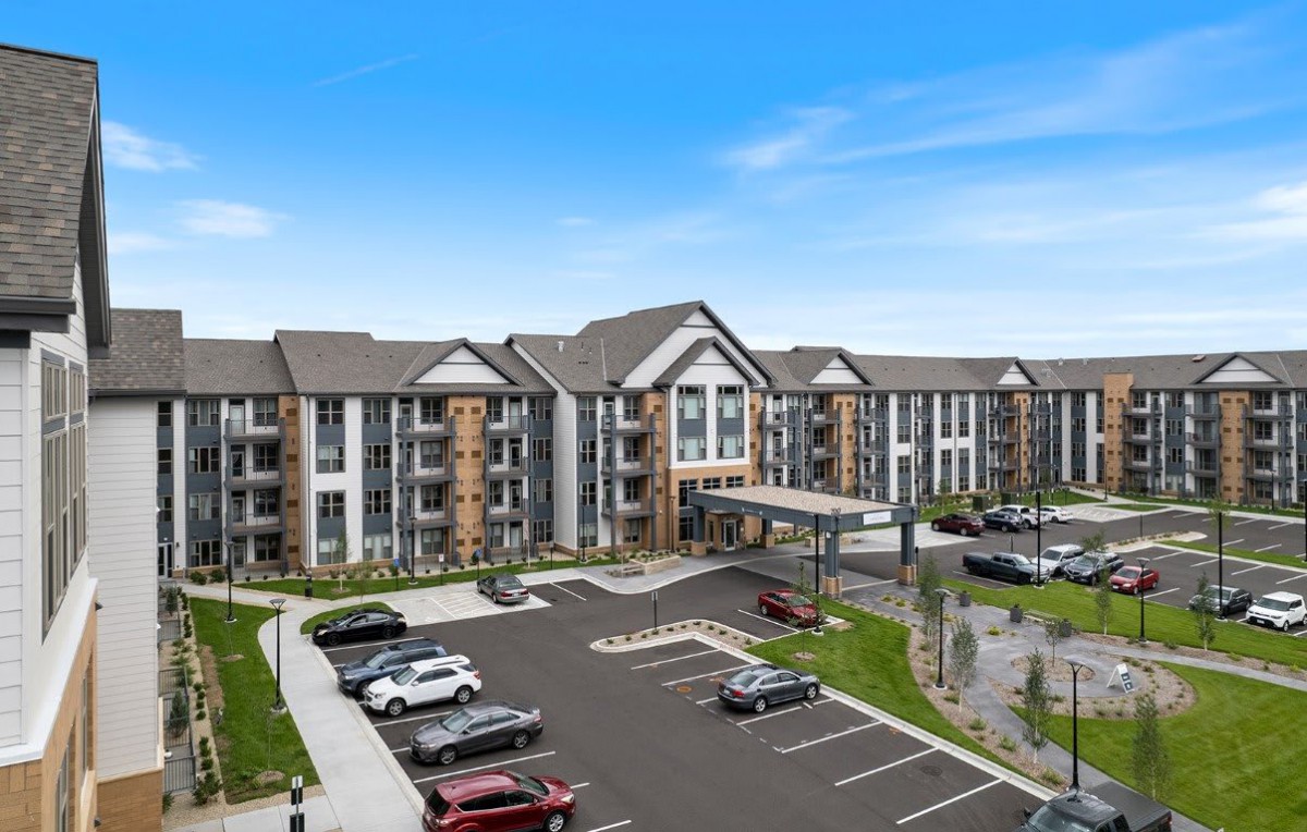 A modern apartment complex with a spacious parking lot in front.