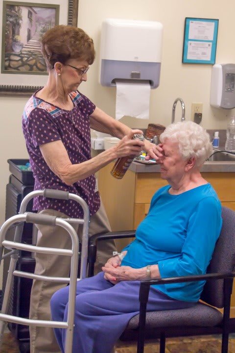 A healthcare worker assists an elderly woman during an eye examination in a clinic setting.