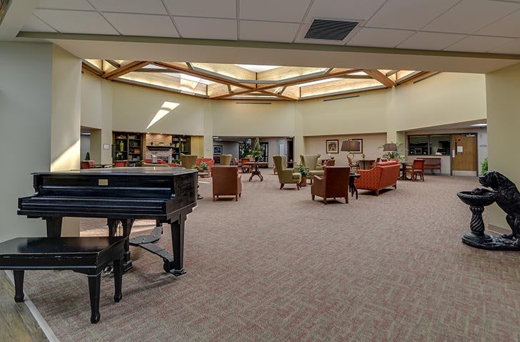 A spacious library interior featuring a grand piano and comfortable seating areas surrounded by bookshelves.