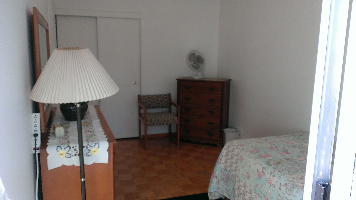 A minimalist bedroom with essential furniture including a lamp, dresser, chair, and bed.