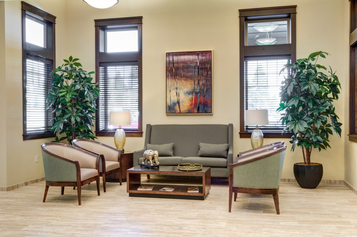 A cozy living room area featuring a sofa, two armchairs, a coffee table, indoor plants, and decorative artwork.