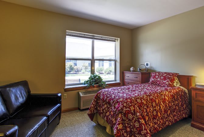 A cozy bedroom with a single bed, wooden dresser, and large window bringing in natural light.